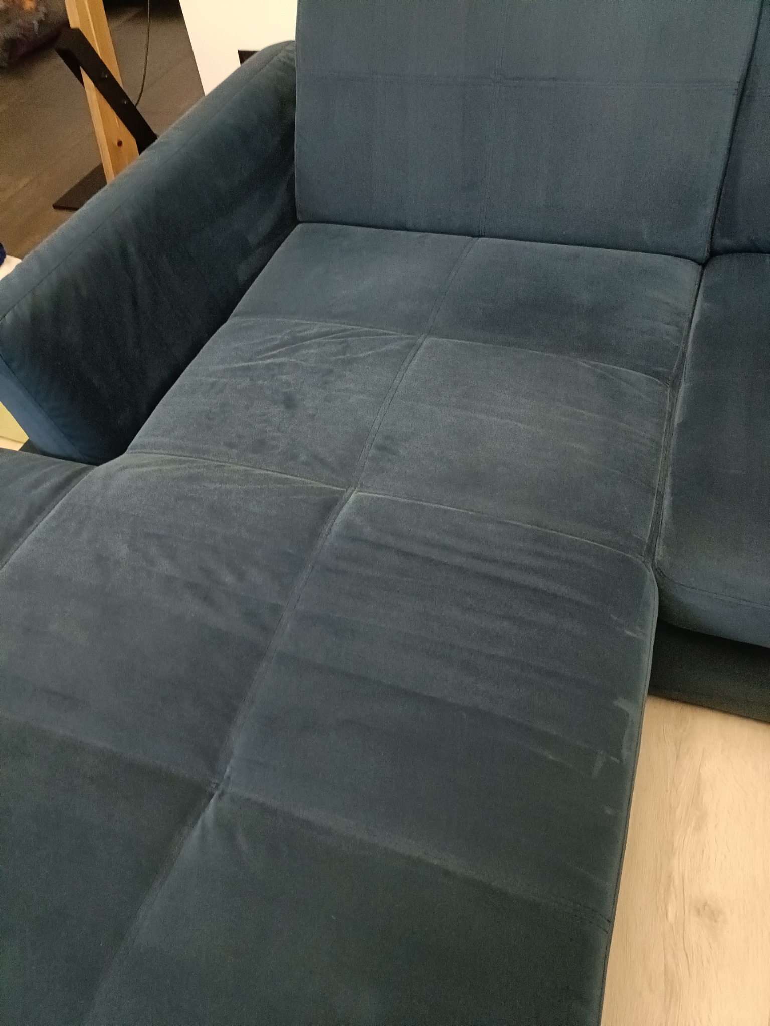 Ciemnoniebieska, narożna kanapa z widocznymi plamami, sugerującymi potrzebę odświeżenia, na jasnej podłodze.