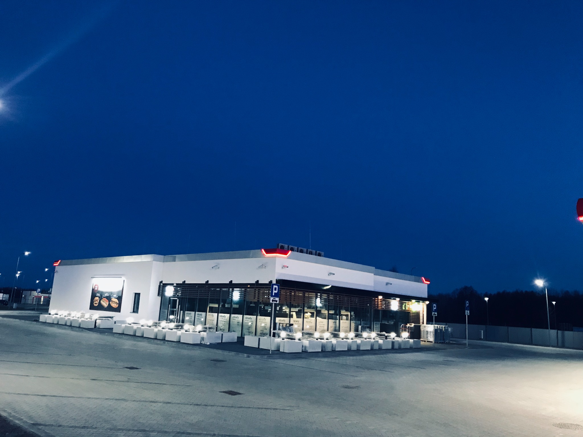 Nowoczesny, parterowy budynek usługowy z dużymi oknami i oświetleniem zewnętrznym, sfotografowany o zmierzchu.