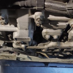 Anton Stovba - Olej silnikowy spływający z odkręconego korka spustowego do czarnego pojemnika podczas wymiany oleju w silniku samochodowym, widok od dołu.