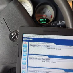 Diagnostyka samochodowa: tablet z uruchomionym programem diagnostycznym Autocom, wyświetlającym brak kodów usterek, na tle kierownicy i deski rozdzielczej samochodu.