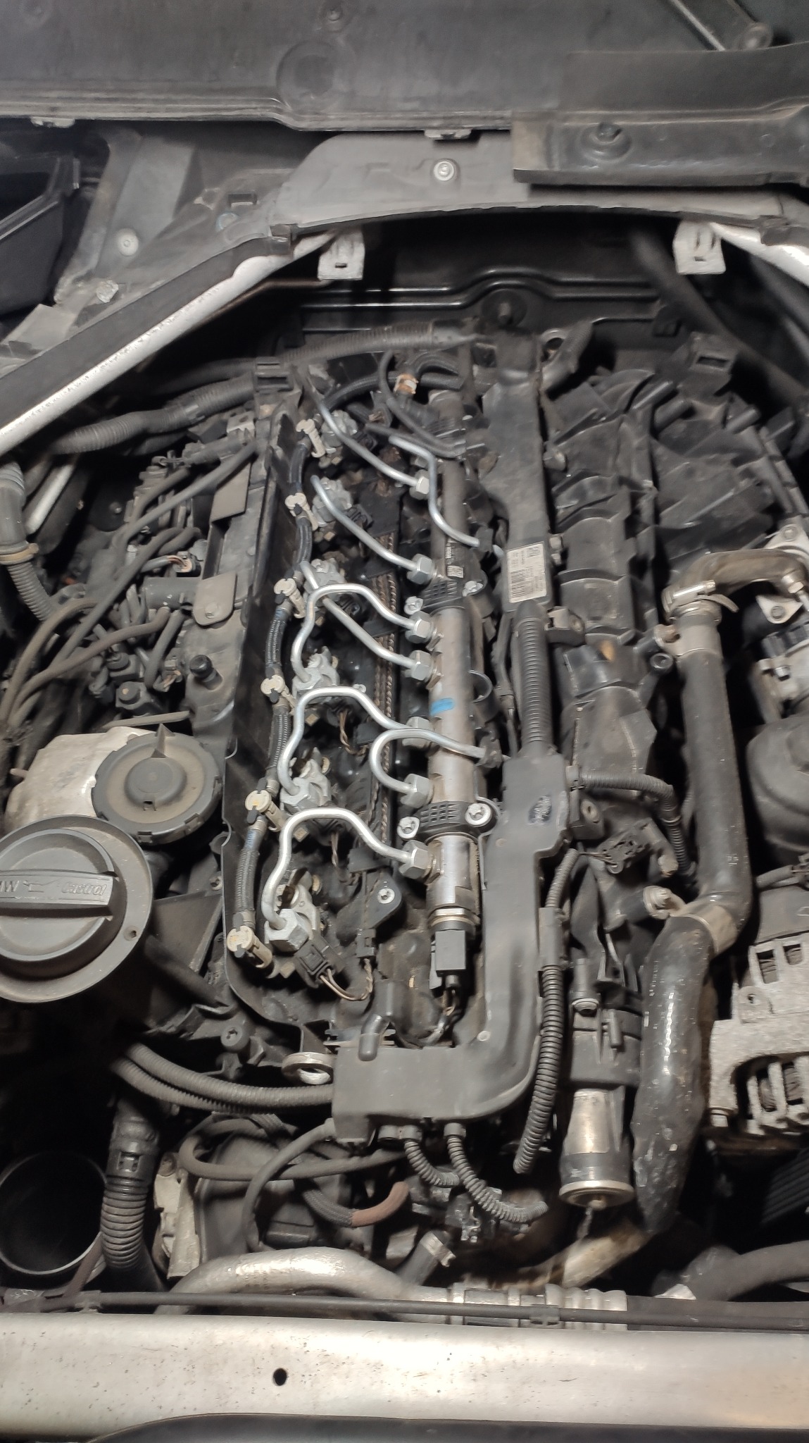 Widok z góry na silnik samochodowy z widocznymi przewodami paliwowymi i osprzętem, w trakcie prac serwisowych.