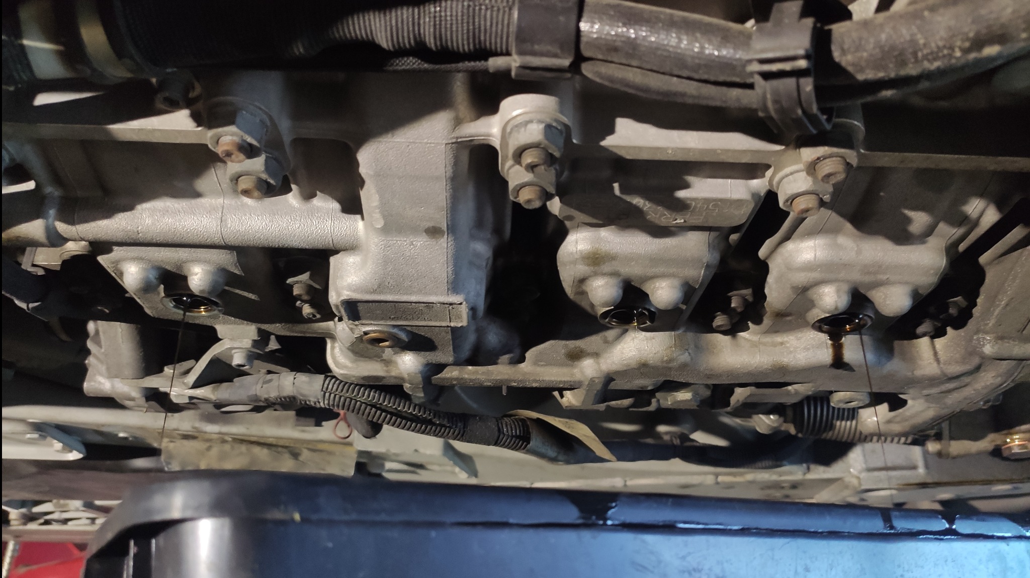 Olej silnikowy spływający z odkręconego korka spustowego do czarnego pojemnika podczas wymiany oleju w silniku samochodowym, widok od dołu.