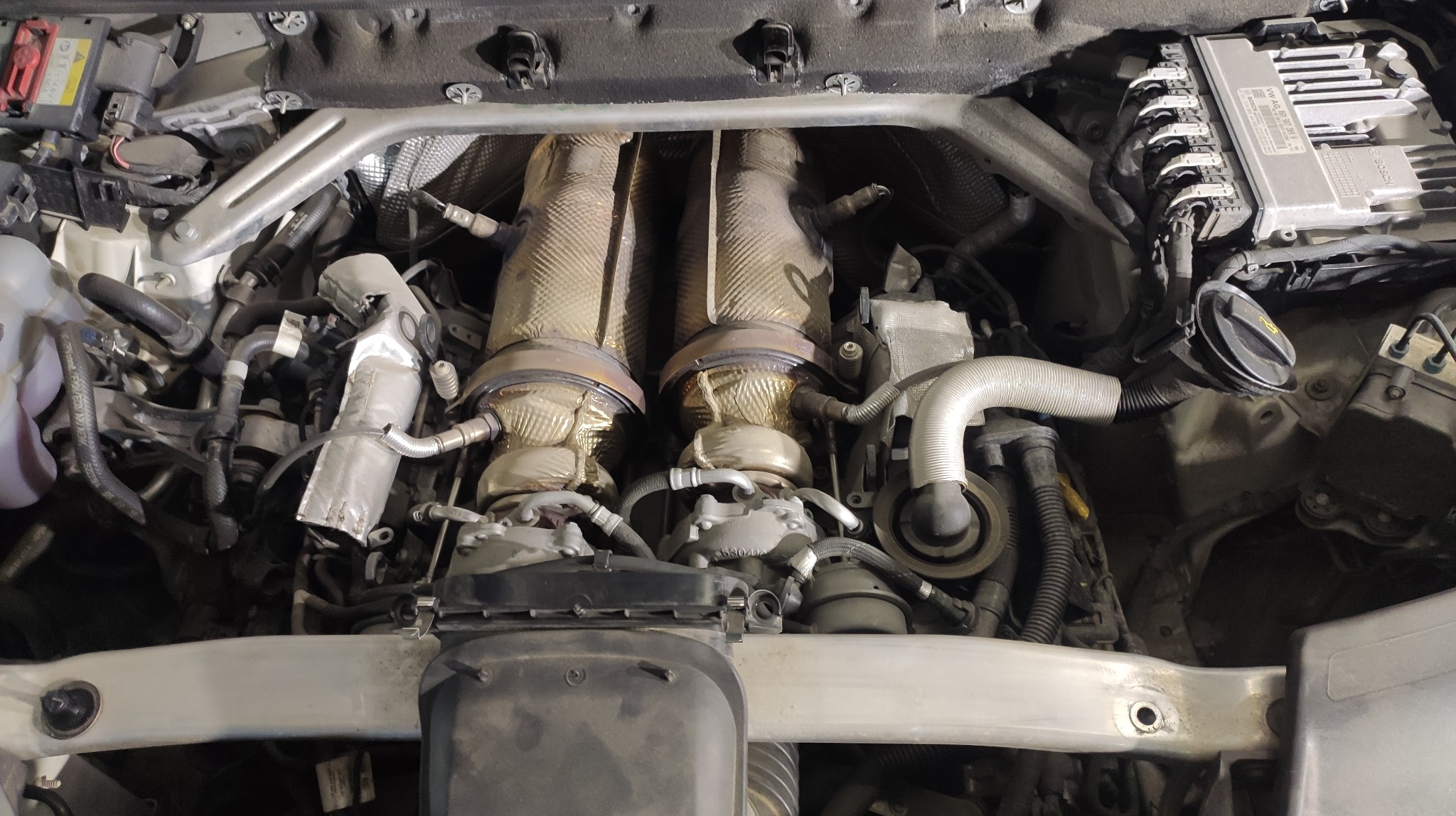 Widok z góry na skomplikowany silnik samochodowy z widocznymi turbosprężarkami owiniętymi w izolację termiczną, liczne przewody i elementy elektroniczne pod maską.