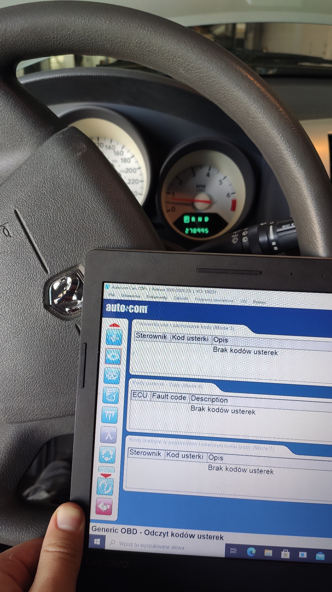 Diagnostyka samochodowa: tablet z uruchomionym programem diagnostycznym Autocom, wyświetlającym brak kodów usterek, na tle kierownicy i deski rozdzielczej samochodu.