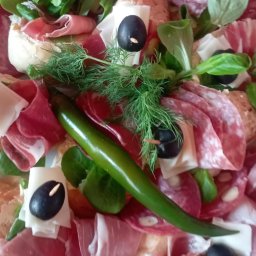 POLSKIE STOWARZYSZENIE RODAK - Dekoracyjna taca z przekąskami: wędliny, sery, oliwki nadziewane na wykałaczki, świeże zioła i ostra zielona papryczka.