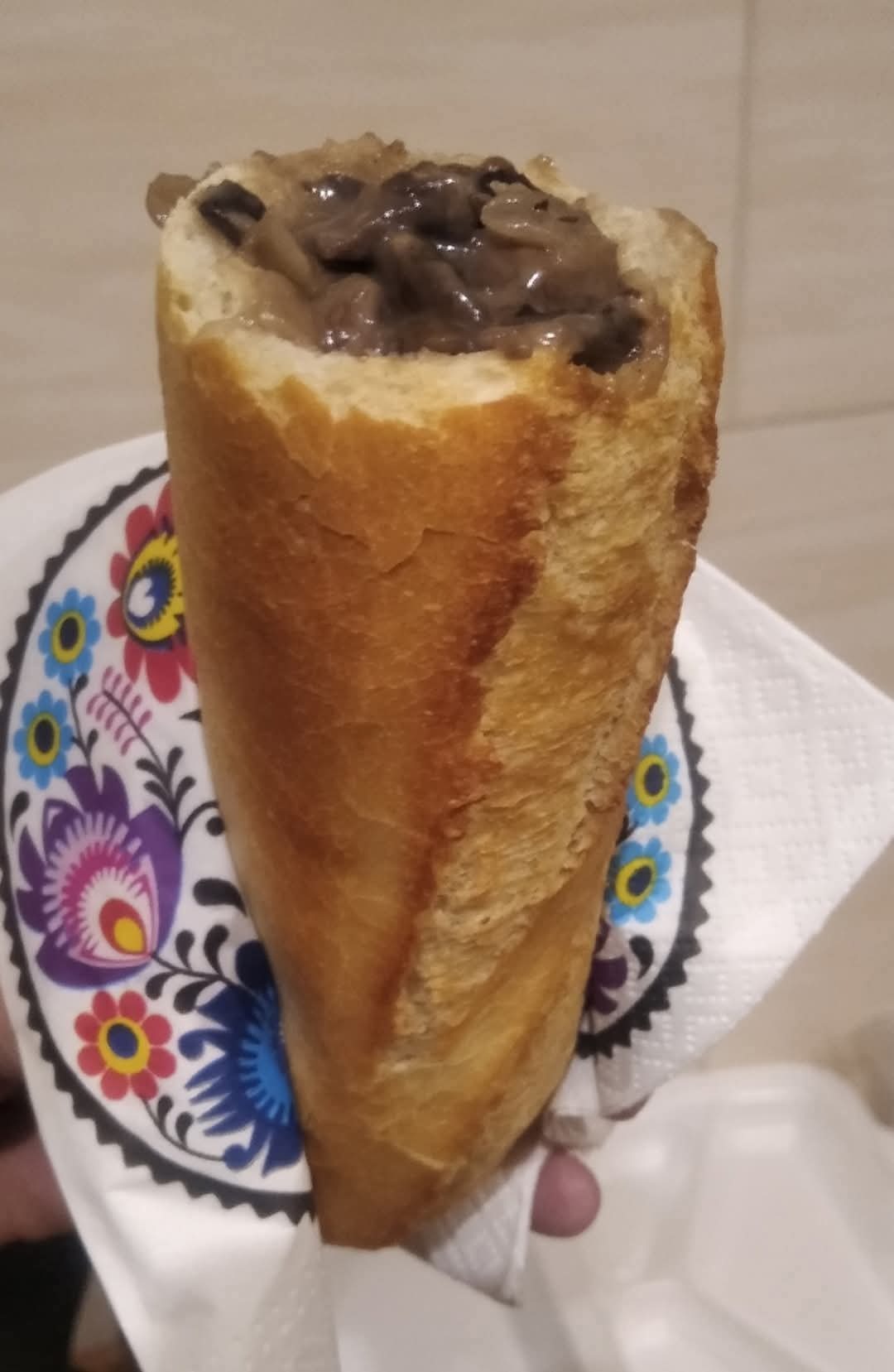 Baguette faszerowana grzybami, podawana na serwetce z ludowym wzorem kwiatowym.