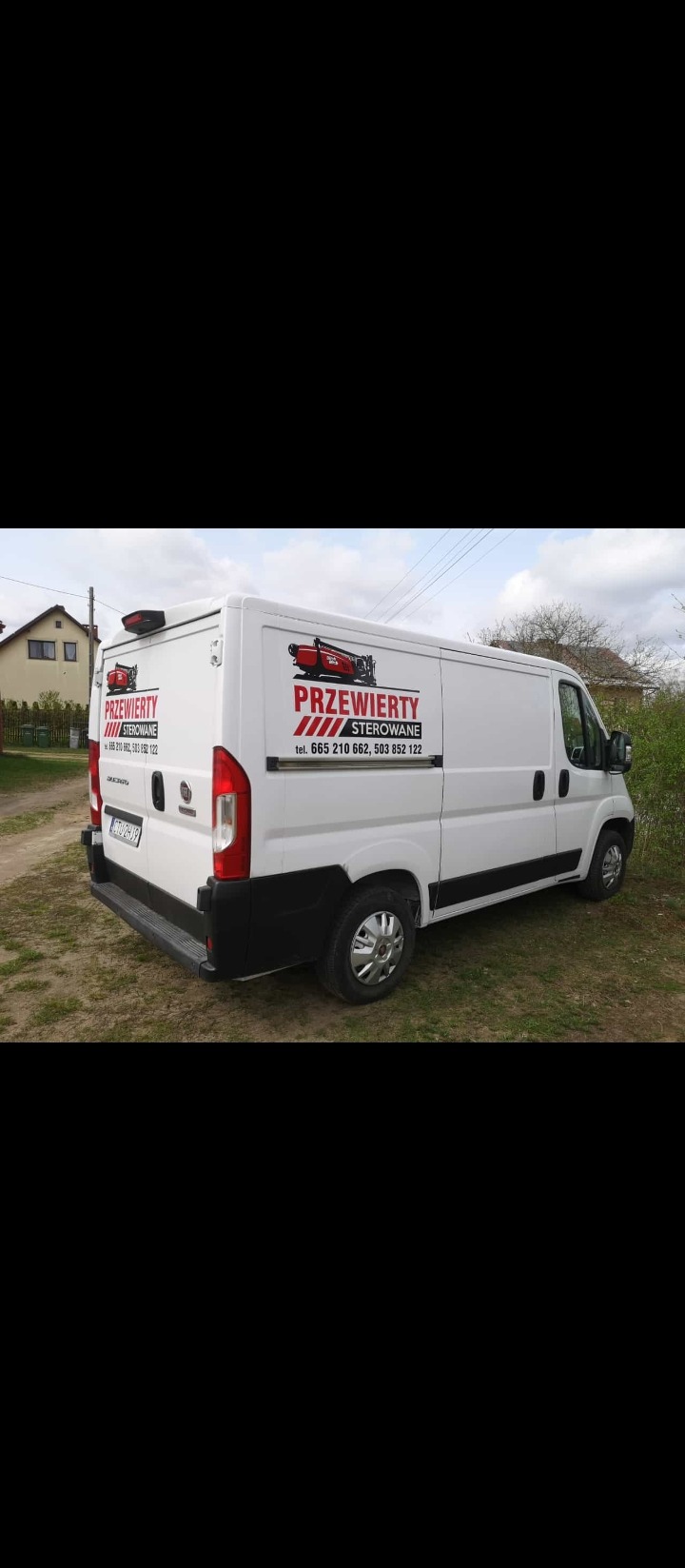 Biały samochód dostawczy z logo firmy świadczącej usługi przewiertów sterowanych, zaparkowany na trawiastym terenie.