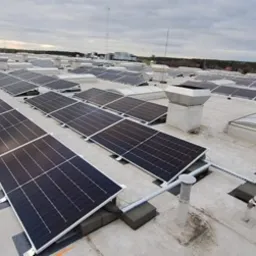 Instalacja fotowoltaiczna na dachu przemysłowym, widok z góry na panele słoneczne z szarym niebem w tle.