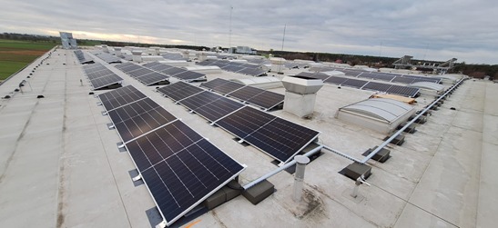 Instalacja fotowoltaiczna na dachu przemysłowym, widok z góry na panele słoneczne z szarym niebem w tle.