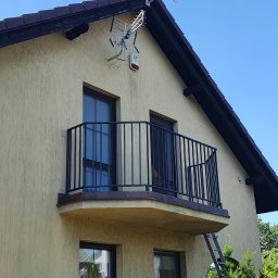 Kamil Aszyk - Zewnętrzny balkon z czarną metalową balustradą, widoczny z dołu, z drabiną opartą o ścianę budynku.