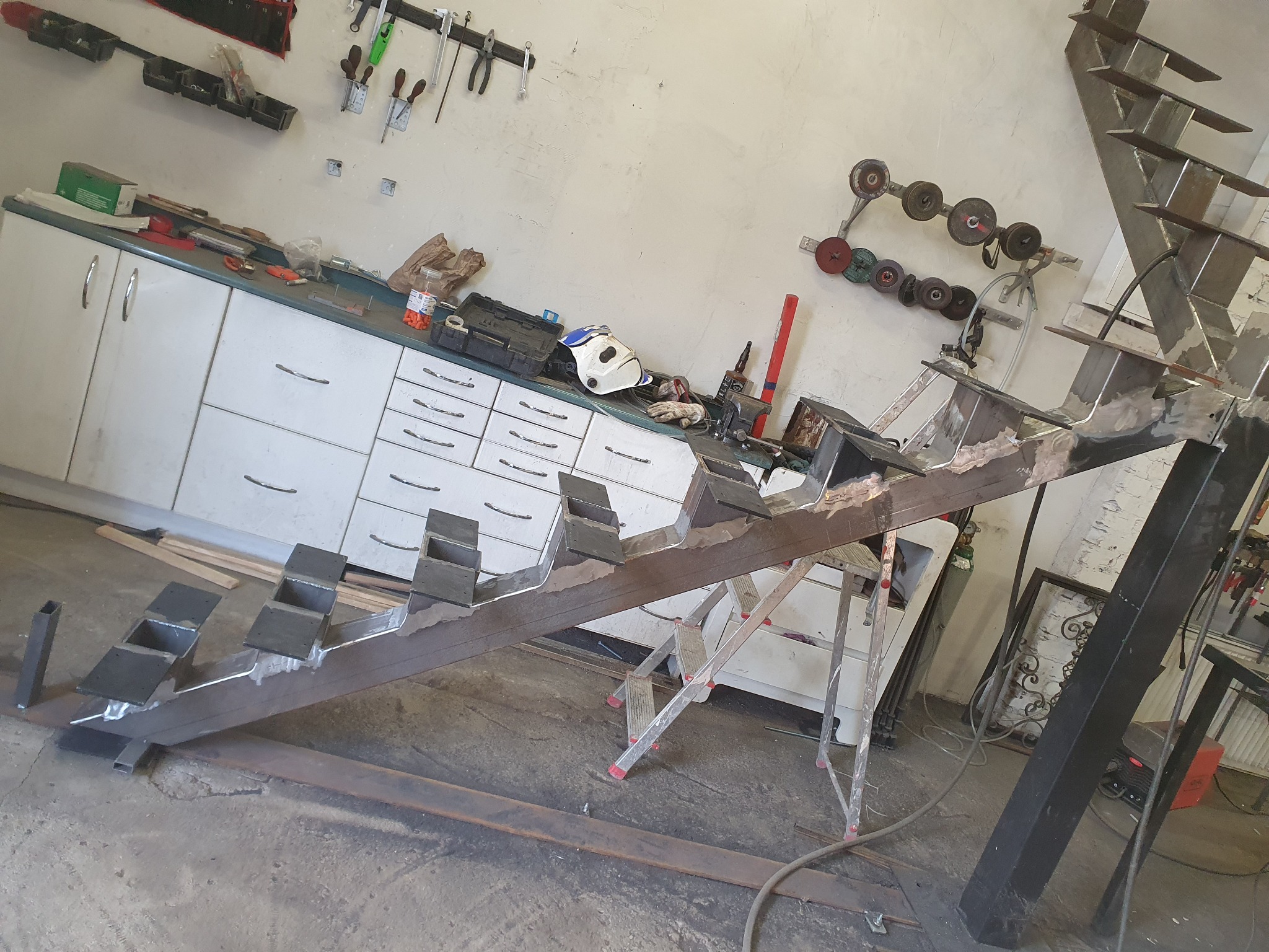 Konstrukcja stalowa schodów w trakcie spawania w warsztacie, widoczne elementy spawane, narzędzia i drabina