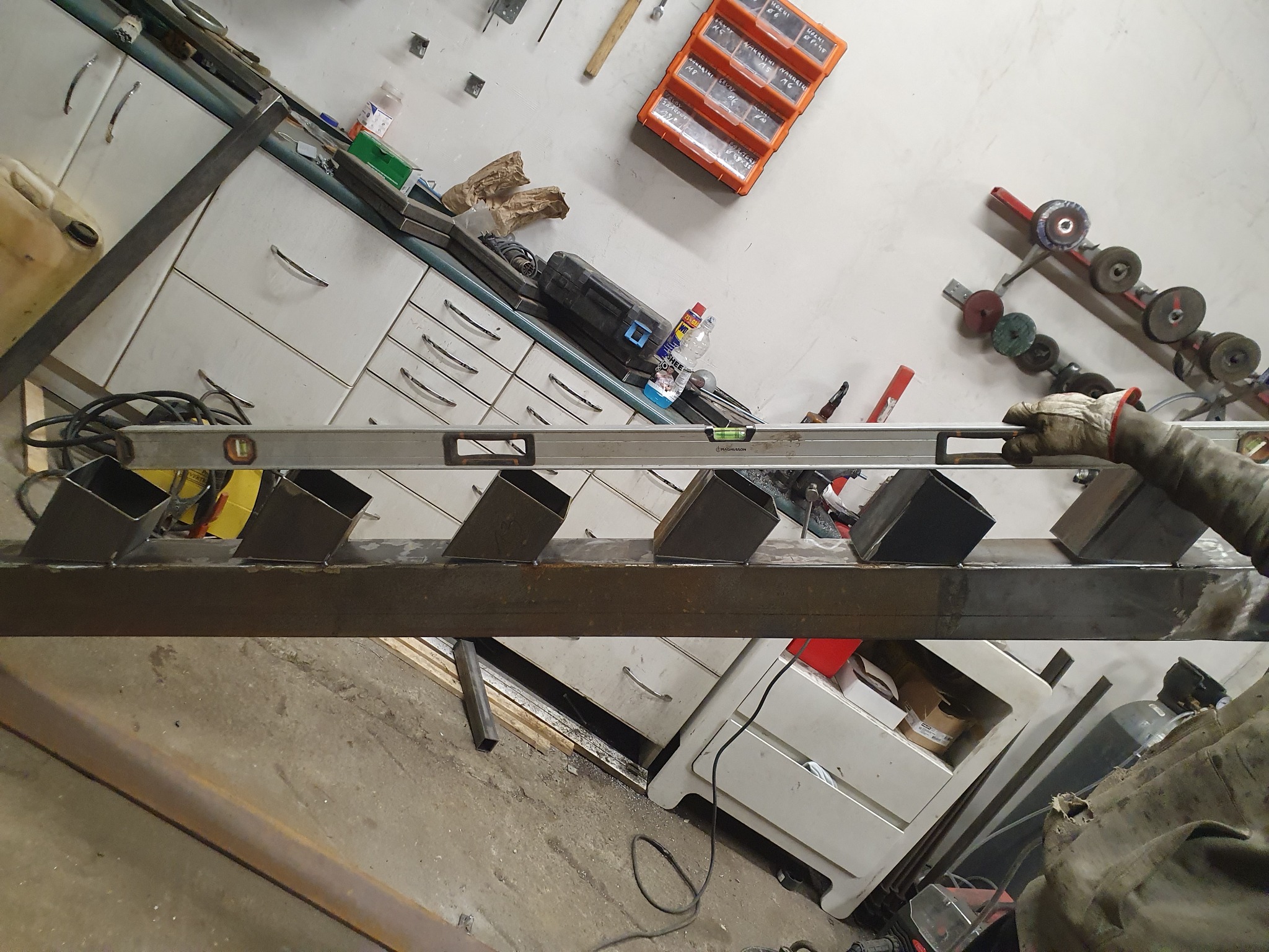 Spawanie konstrukcji metalowej w warsztacie w Pelplinie: przymiarka metalowych elementów schodów z użyciem poziomicy, widoczne narzędzia i akcesoria warsztatowe w tle.