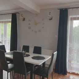 Pasternik - Jasne wnętrze jadalni z białym stołem, czarnymi krzesłami, dużym zegarem ściennym i dekoracyjnymi lampami ściennymi w stylu retro.