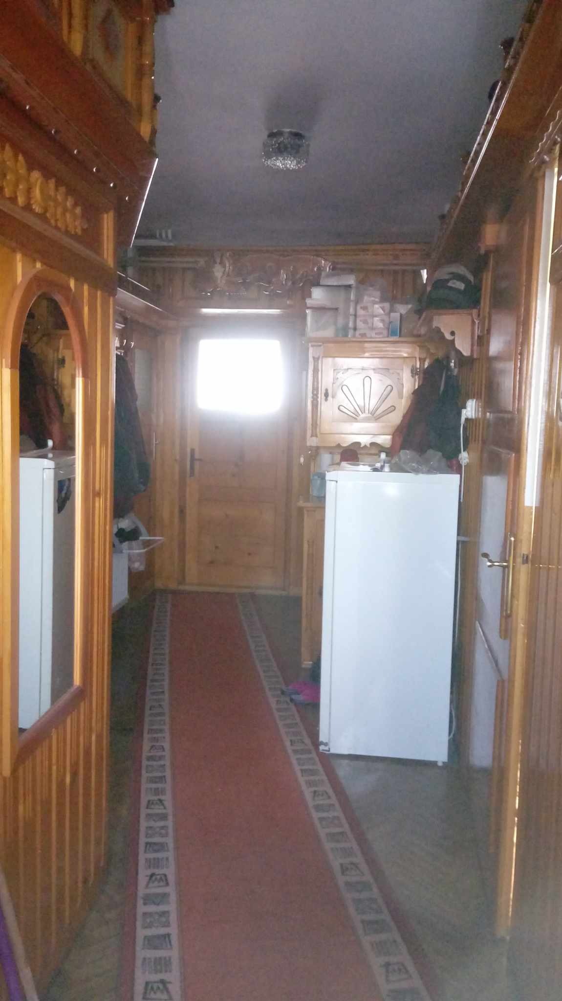 Drewniany przedpokój w stylu góralskim w Zakopanem z białymi lodówkami po bokach, bieżnikiem na podłodze i ozdobnym oświetleniem sufitowym.