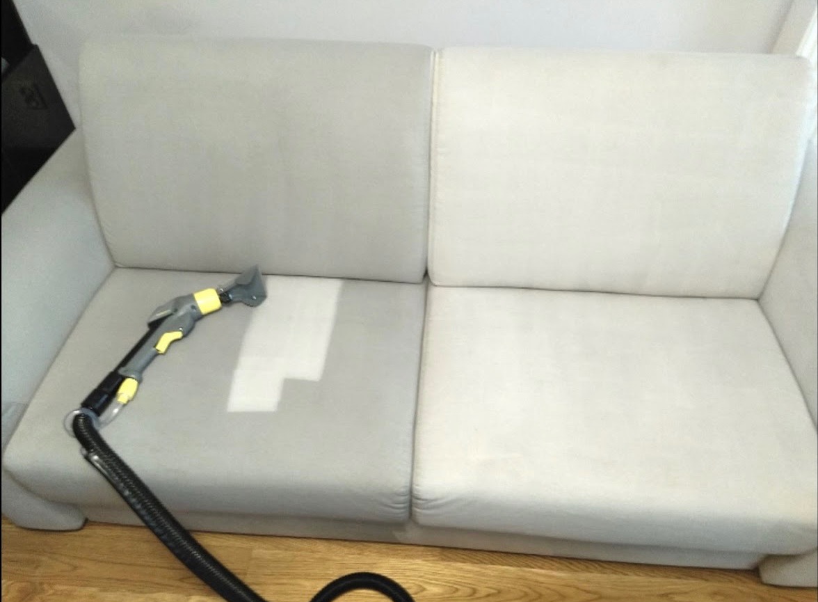 Jasna kanapa w trakcie czyszczenia: widoczna różnica w kolorze między wyczyszczonym a nie wyczyszczonym fragmentem siedziska, z dyszą czyszczącą i wężem na pierwszym planie.