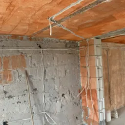 Instalacja elektryczna w surowym wnętrzu: przewody prowadzone po ścianach z cegły i suficie z widoczną konstrukcją, etap prac wykończeniowych.
