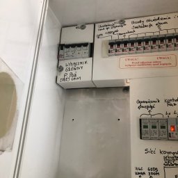 RobertoGreenenergy - Otwarta skrzynka elektryczna z wyłącznikami, bezpiecznikami i opisami odręcznymi, widoczne okablowanie i zabezpieczenia przeciwprzepięciowe.