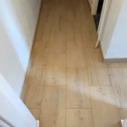 Ułożona podłoga z paneli laminowanych w przedpokoju, widok z góry, z widocznymi listwami przypodłogowymi i fragmentami ścian oraz futryn drzwiowych.