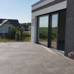 Just Energy Daniel Liebert - Nowoczesny taras wyłożony szarymi płytkami, ze stalową balustradą, widok na okoliczne domy i pola w słoneczny dzień.