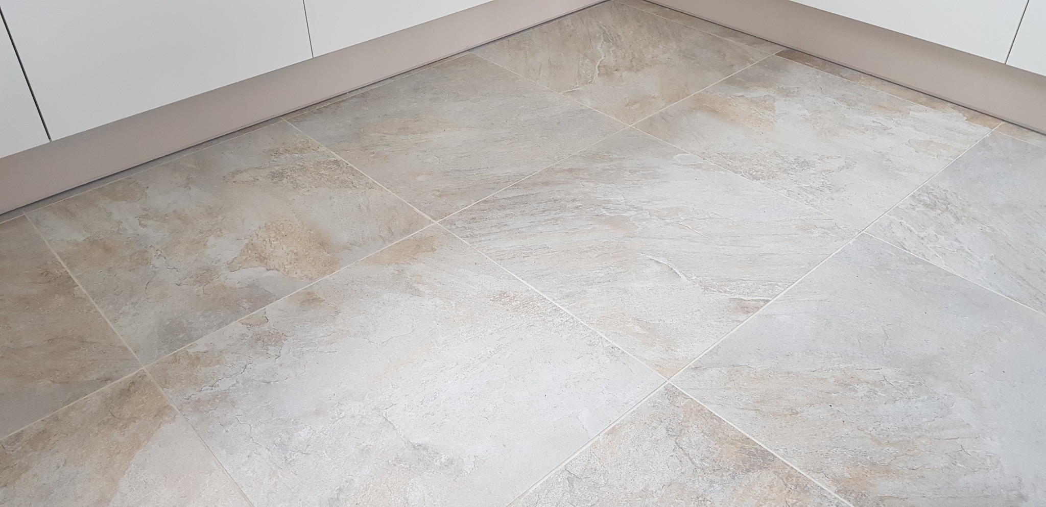 Jasne, beżowo-szare płytki podłogowe, ułożone w kwadraty, widoczne przy białych szafkach w pomieszczeniu w Cedrach Wielkich.