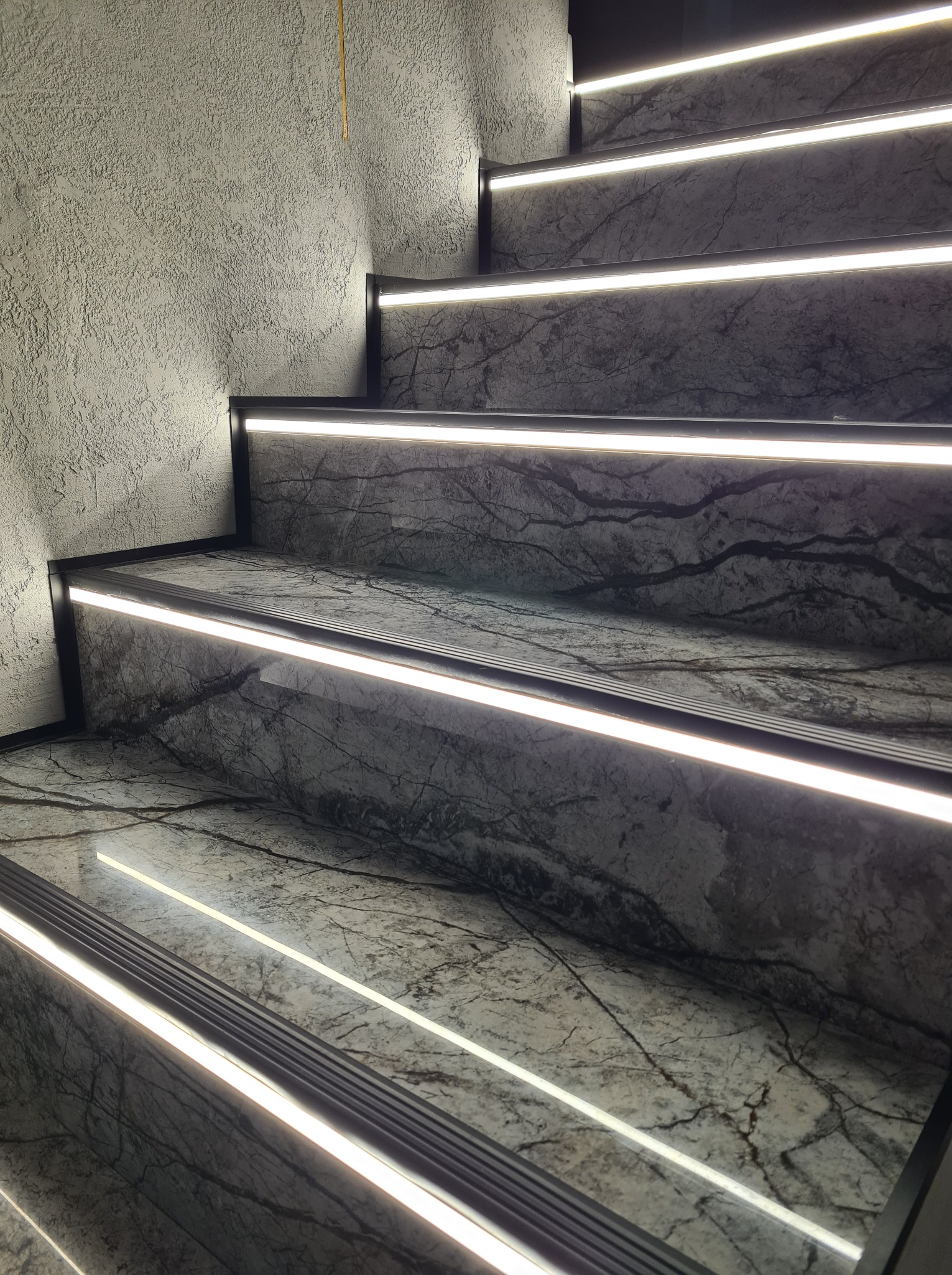 Schody wyłożone marmurem z podświetleniem LED, widok z dołu, szara ściana z fakturą.