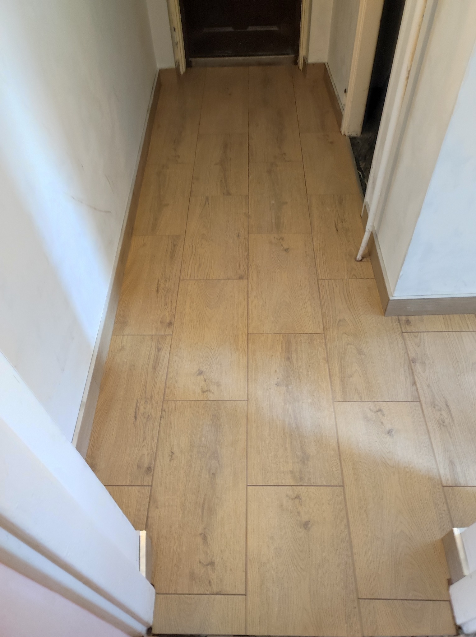 Ułożona podłoga z paneli laminowanych w przedpokoju, widok z góry, z widocznymi listwami przypodłogowymi i fragmentami ścian oraz futryn drzwiowych.