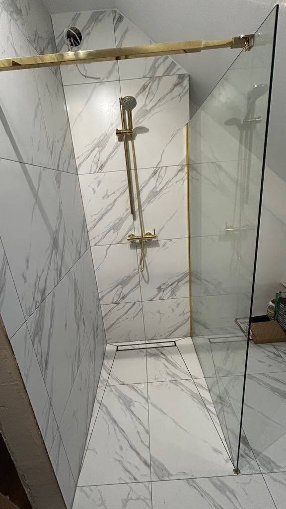 Nowoczesna kabina prysznicowa walk-in z białymi płytkami imitującymi marmur, złotymi akcentami i odpływem liniowym, zrealizowana w Cedrach Wielkich.