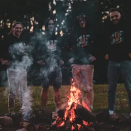 Czteroosobowy zespół w ciemnych bluzach z logo firmy, stojący wokół ogniska w plenerze, z dymem unoszącym się w powietrzu, sugerujący integrację zespołu IT.