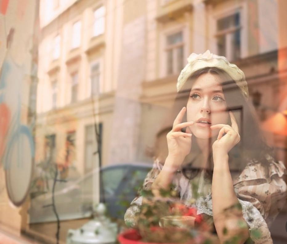 Portret kobiety w koronie, odbicie w oknie kawiarni z widokiem na ulicę i budynki.