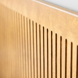 IXIDO Sp. z o.o. - Drewniana płyta z pionowymi, równoległymi wycięciami, widoczna pod kątem, z logo hostelu w prawym dolnym rogu.