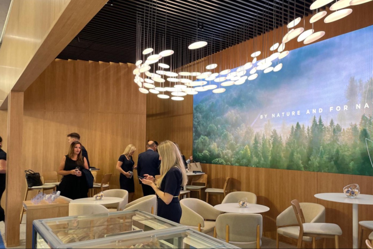 Nowoczesna aranżacja biurowa z drewnianymi panelami, oświetleniem punktowym i dużym panelem z motywem leśnym, widoczne osoby w tle.