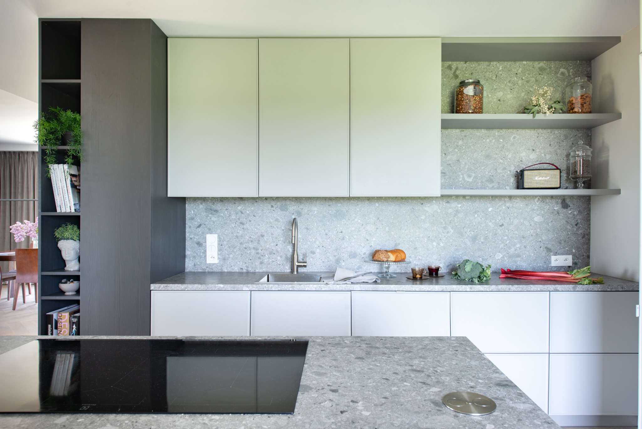 Nowoczesna kuchnia w odcieniach szarości i bieli z blatem z lastryko, wyposażona w płytę indukcyjną, z otwartymi półkami z dekoracjami i produktami spożywczymi.