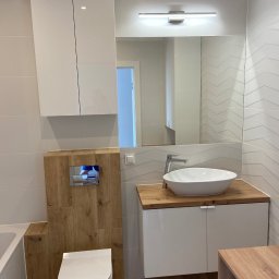 HS MEBLE Hubert Słowikowski - Nowoczesna łazienka z białą armaturą i drewnianymi akcentami. Umywalka nablatowa, szafka pod umywalkę i wisząca szafka tworzą spójną całość.  Ściana z wzorem w jodełkę.