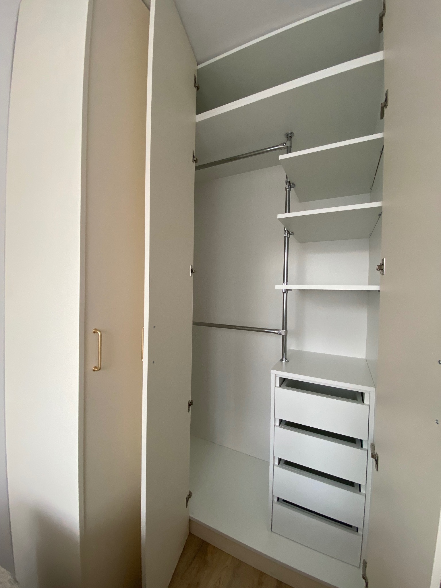 Jasna szafa wnękowa z otwartymi drzwiami, widoczne półki i szuflady. Minimalistyczny design, złote uchwyty. Widok z bliska na wnętrze szafy.