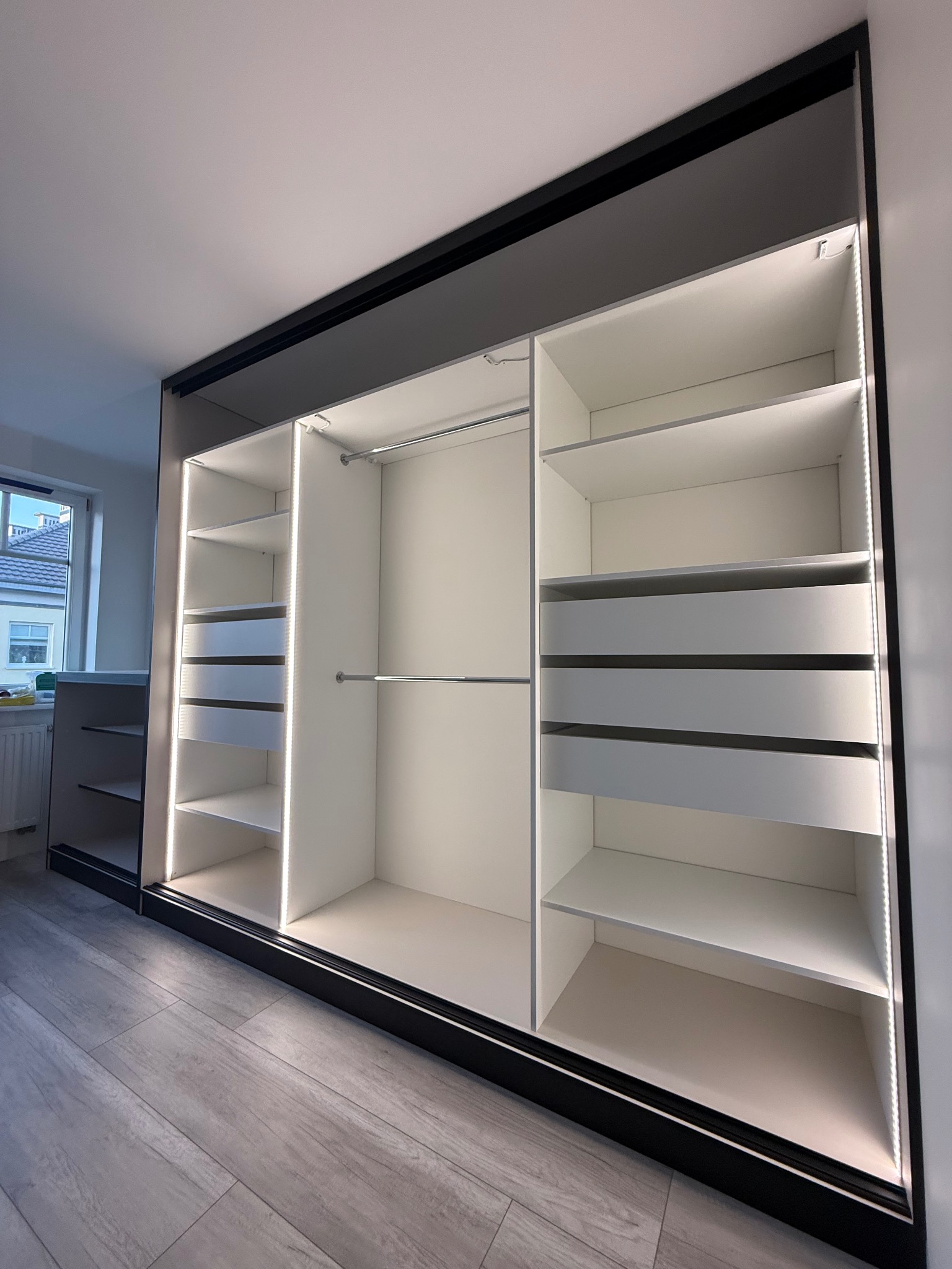 Nowoczesna szafa wnękowa z przesuwnymi drzwiami, oświetleniem LED i szufladami. Widok z dołu, ukazujący przestronne wnętrze i minimalistyczny design.