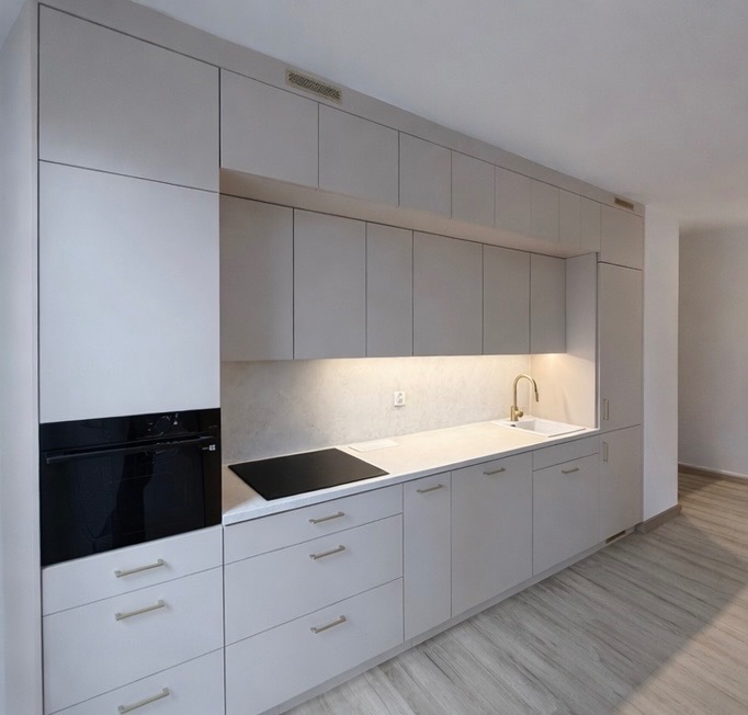 Jasnoszara kuchnia na wymiar z zabudową po sufit, złota bateria, płyta indukcyjna i piekarnik w zabudowie. Minimalistyczny design, oświetlenie LED pod szafkami.