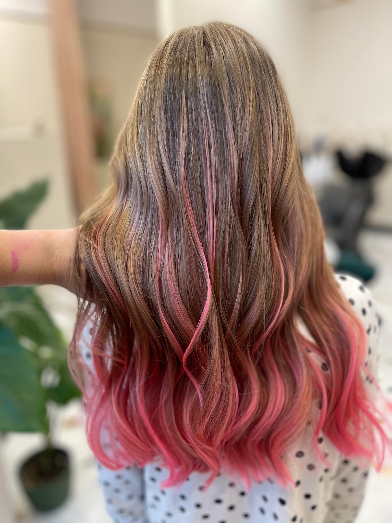 Brązowe włosy z różowymi pasemkami i końcówkami, widok z tyłu, delikatne fale, stylizacja wykonana w salonie fryzjerskim.