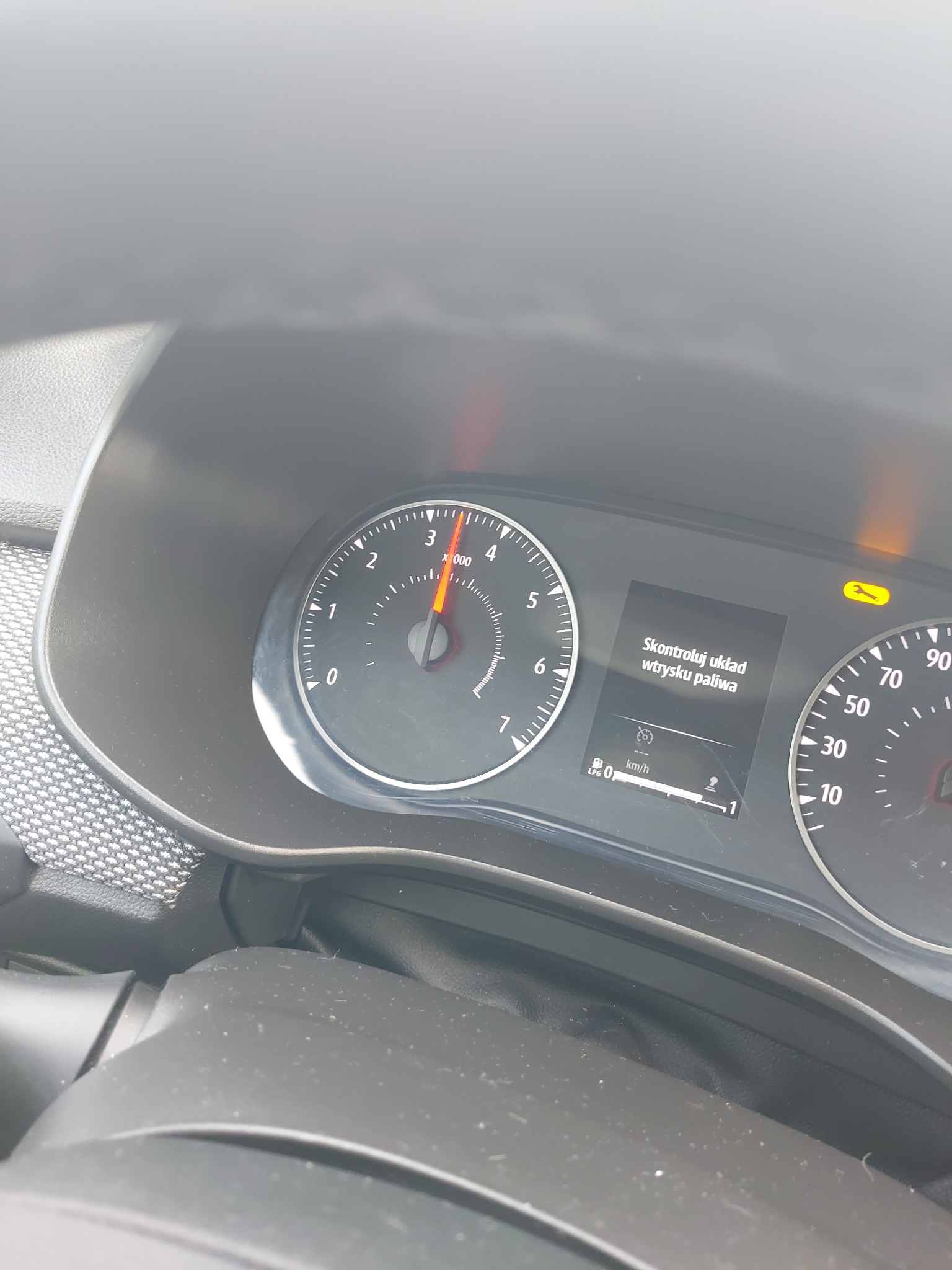 Deska rozdzielcza samochodu z włączoną kontrolką awarii układu wtrysku paliwa i wskazówką obrotomierza na 3000 obr./min.