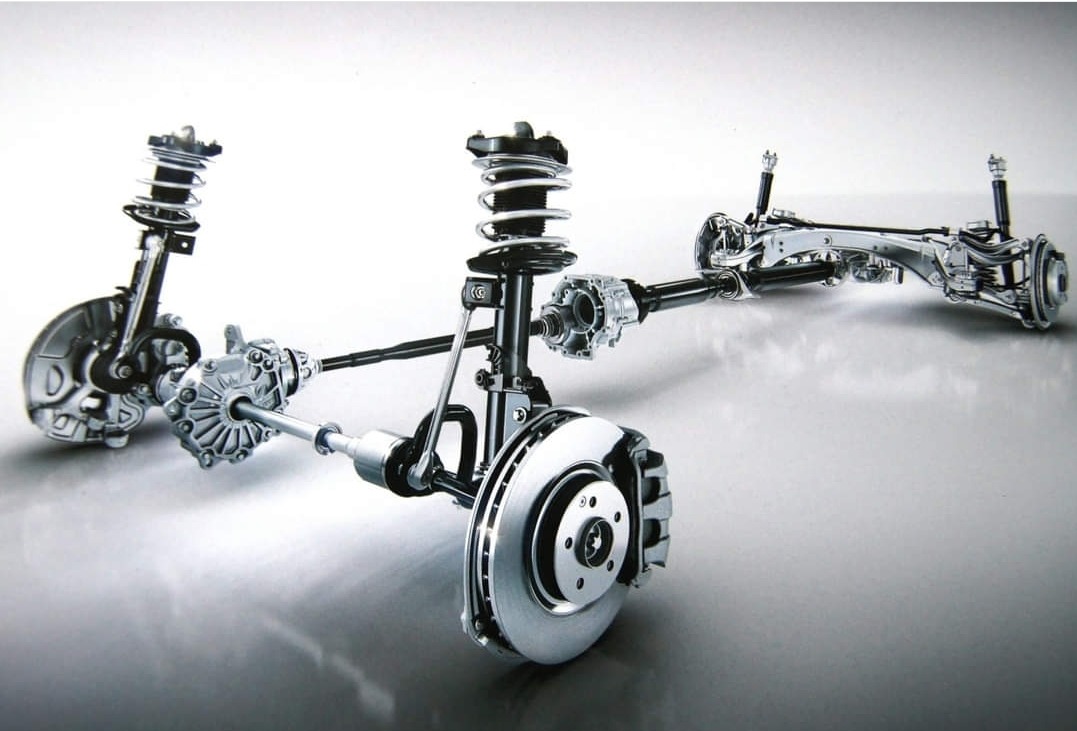 Schematyczny widok zawieszenia samochodowego z amortyzatorami, sprężynami i tarczami hamulcowymi na jasnym tle.