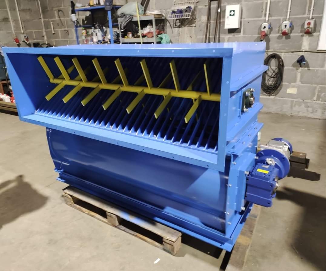 Niebieski mieszalnik przemysłowy z żółtymi elementami mieszającymi, umieszczony na drewnianej palecie w hali produkcyjnej.