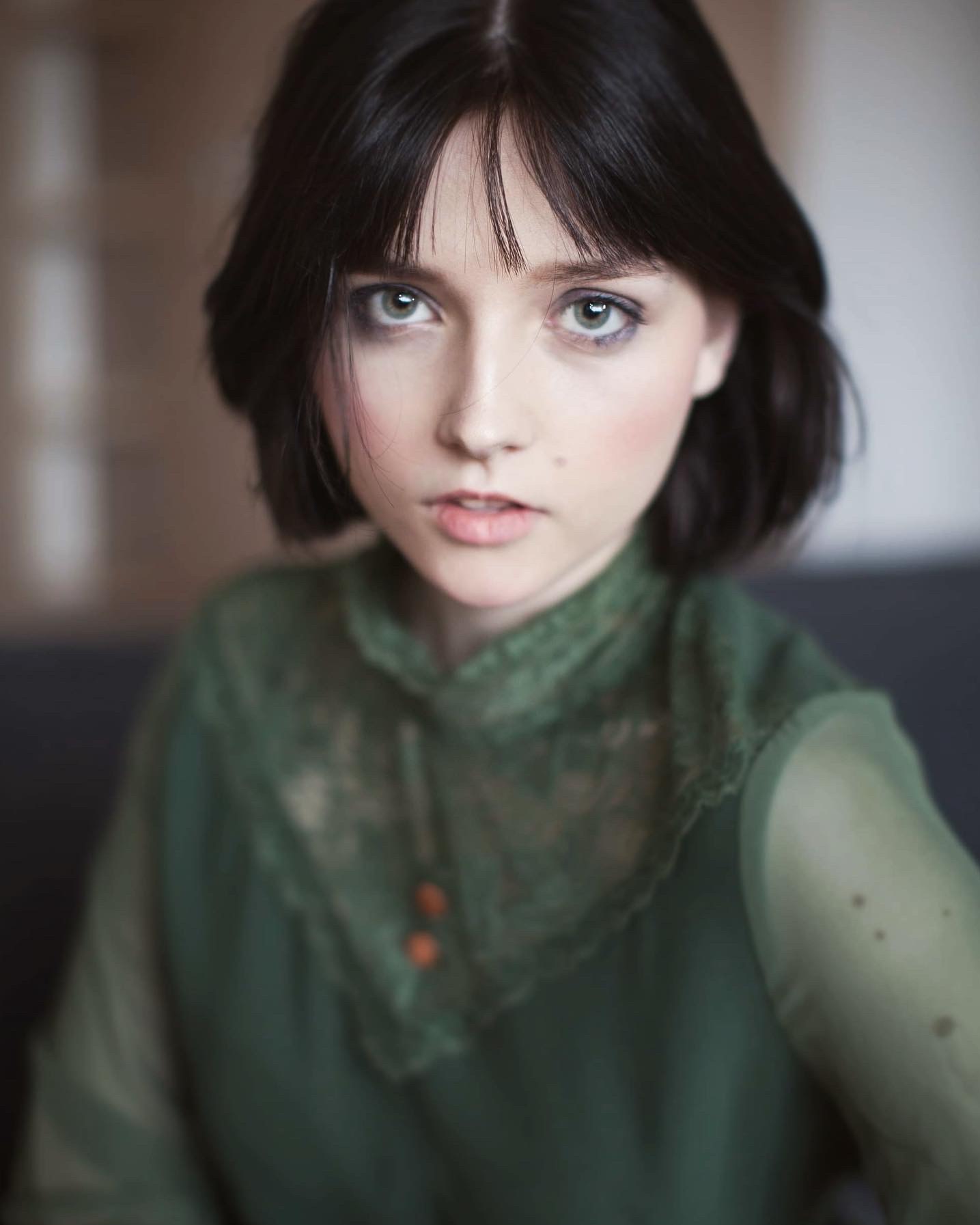 Portret młodej kobiety z krótkimi, ciemnymi włosami i zielonymi oczami, ubrana w zieloną bluzkę z koronkowym kołnierzem, skierowana wprost do kamery.