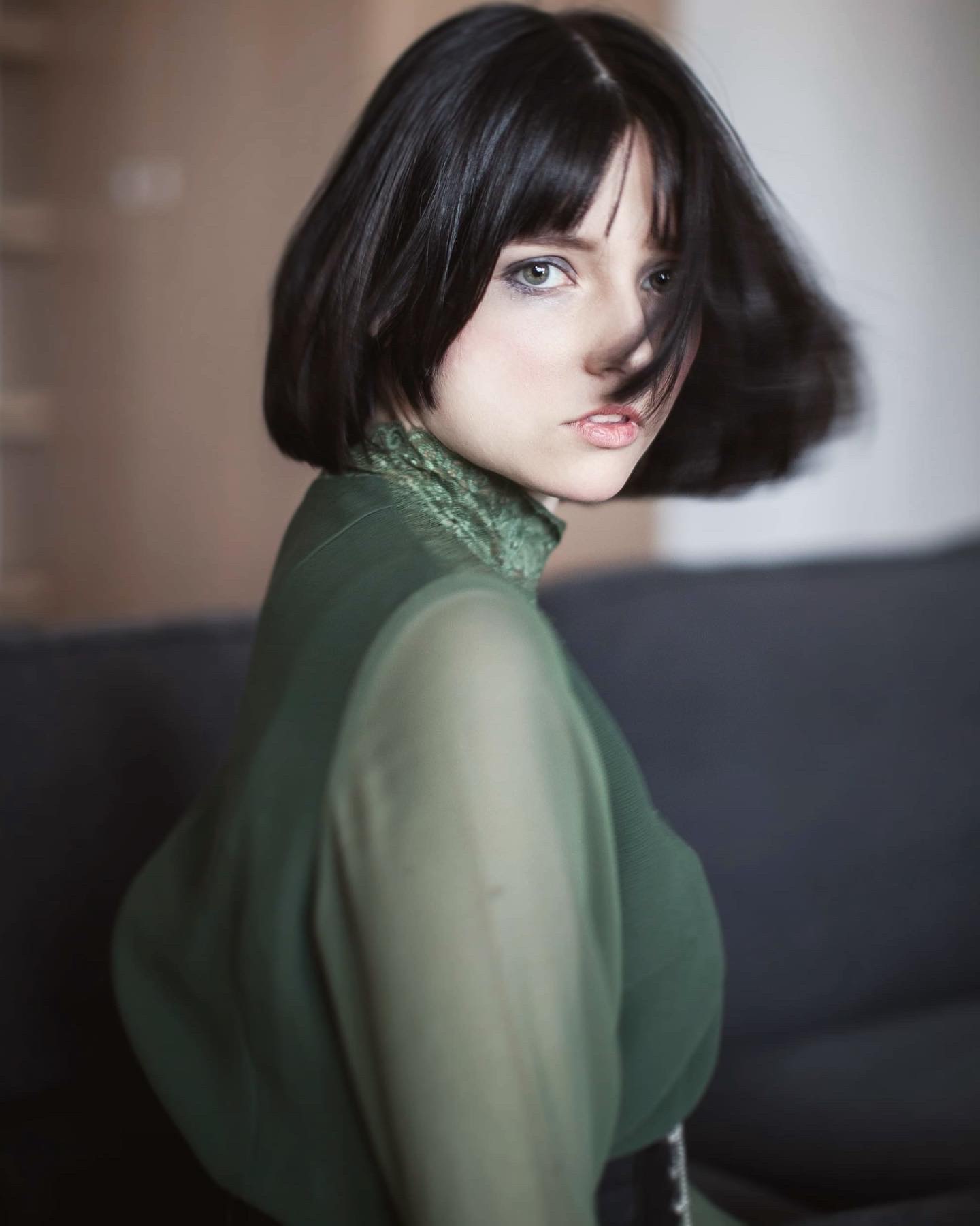 Portret kobiety z krótkimi, czarnymi włosami, ubrana w zieloną bluzkę z golfem, patrząca przez ramię.