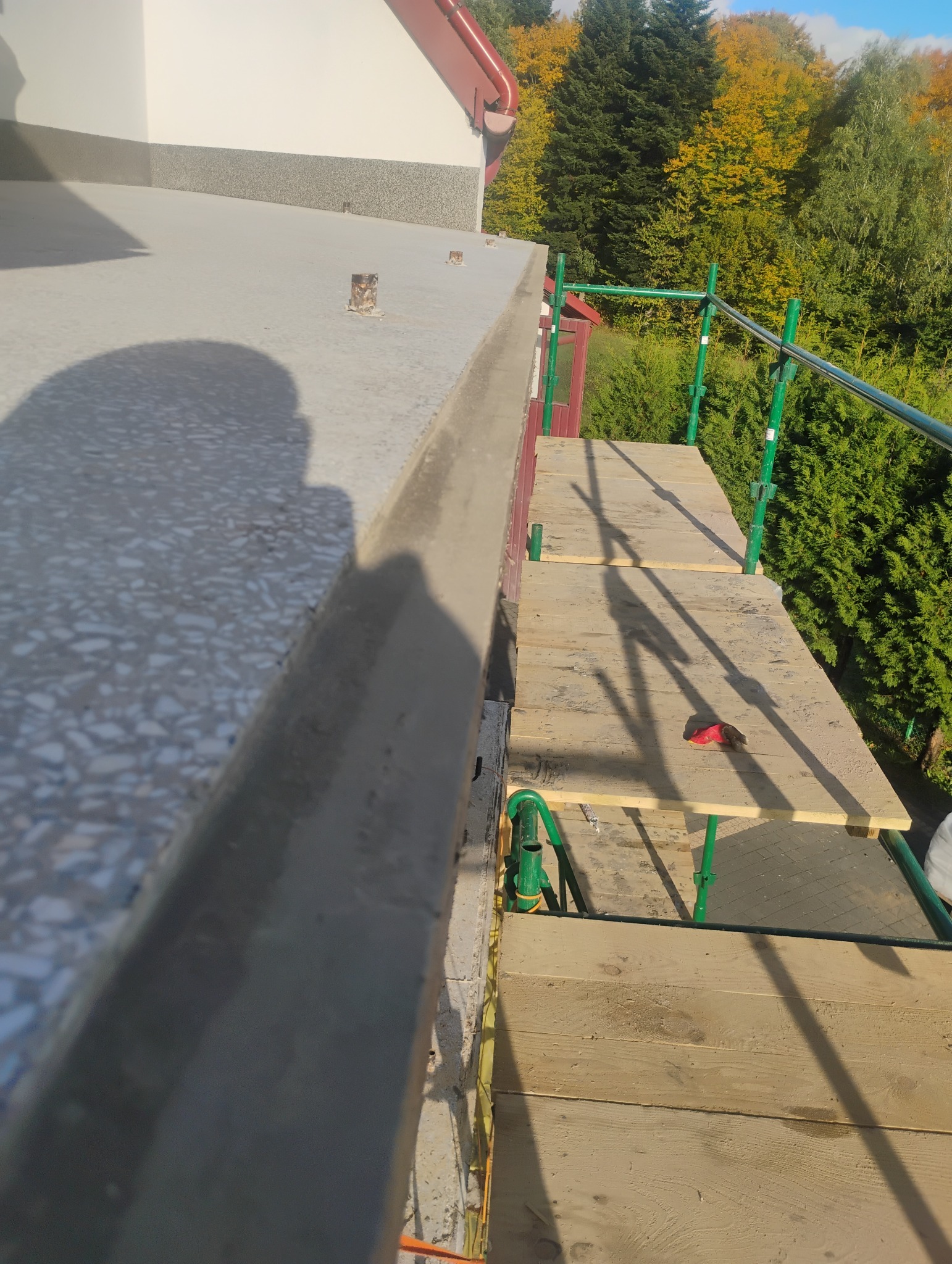 Wykończony balkon z terazzo i świeżo nałożonym szarym tynkiem, widok z rusztowania na tle zieleni.