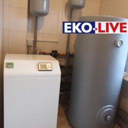 P.W.Eko-Live J.Krzysztofczyk - Kompaktowa kotłownia z pompą ciepła EKO-PCS w pomieszczeniu z ceramiczną okładziną ścienną, widoczne zbiorniki wyrównawcze i zasobnik ciepłej wody z logo EKO-LIVE.