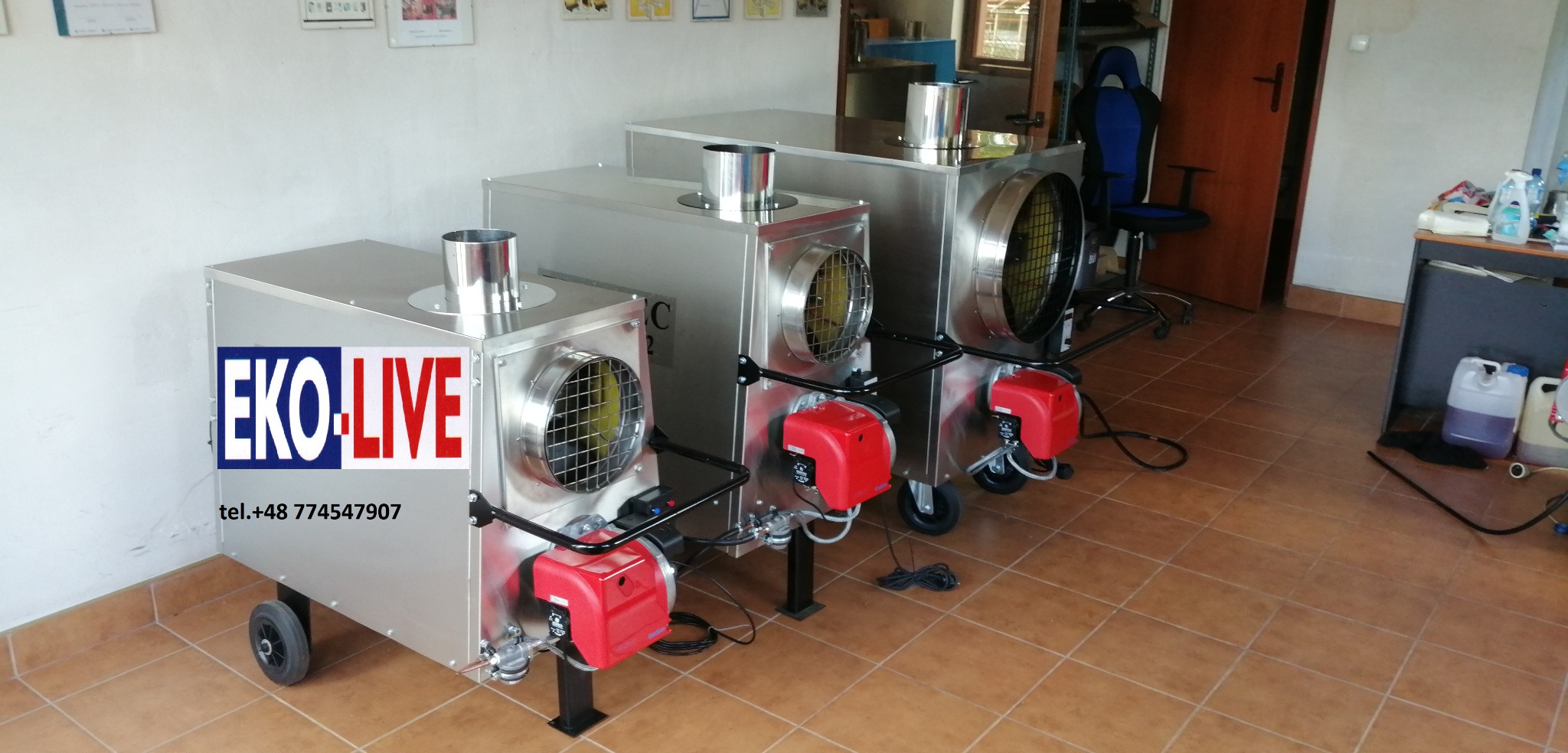 Trzy mobilne nagrzewnice powietrza EKO-LIVE ze stali nierdzewnej, z czerwonymi palnikami, ustawione na brązowej podłodze z płytek, widoczny numer telefonu na obudowie pierwszej nagrzewnicy.