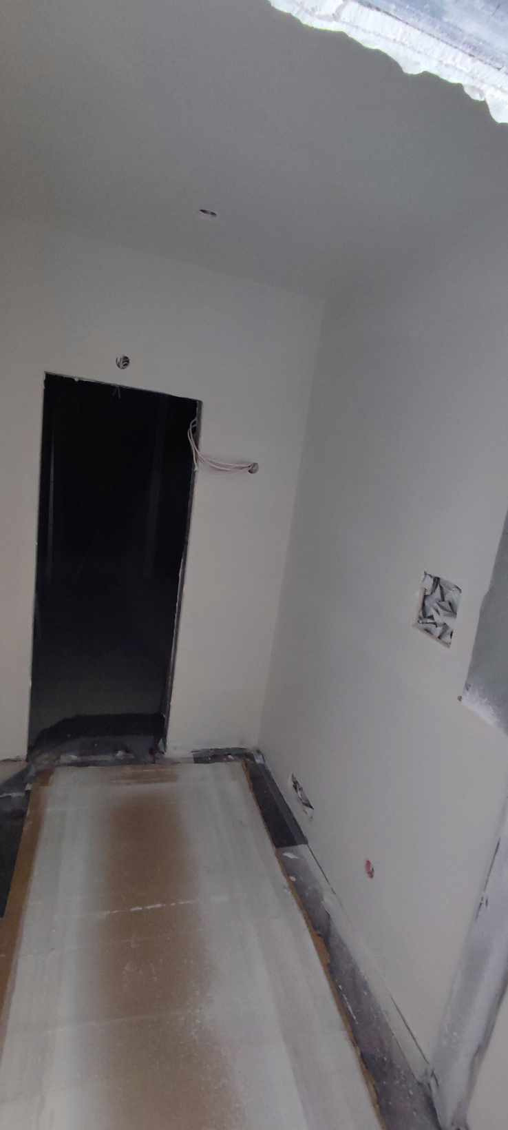 Przygotowane do malowania wnętrze z widocznymi przewodami elektrycznymi wystającymi ze ściany obok ościeżnicy.