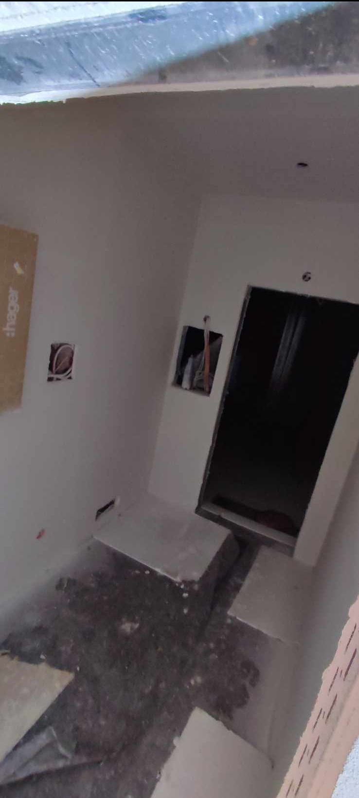 Wnętrze w trakcie prac wykończeniowych: ściany przygotowane do malowania, widoczne puszki elektryczne i wnęka z instalacją, podłoga częściowo zabezpieczona.