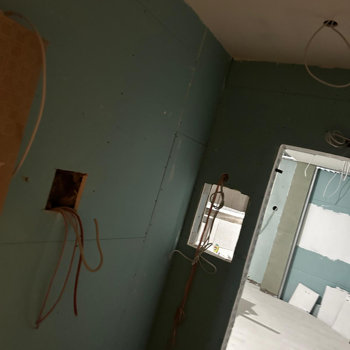 Wnętrze w trakcie szpachlowania ścian gipsowo-kartonowych z widocznymi przewodami elektrycznymi wystającymi z otworów w ścianie.