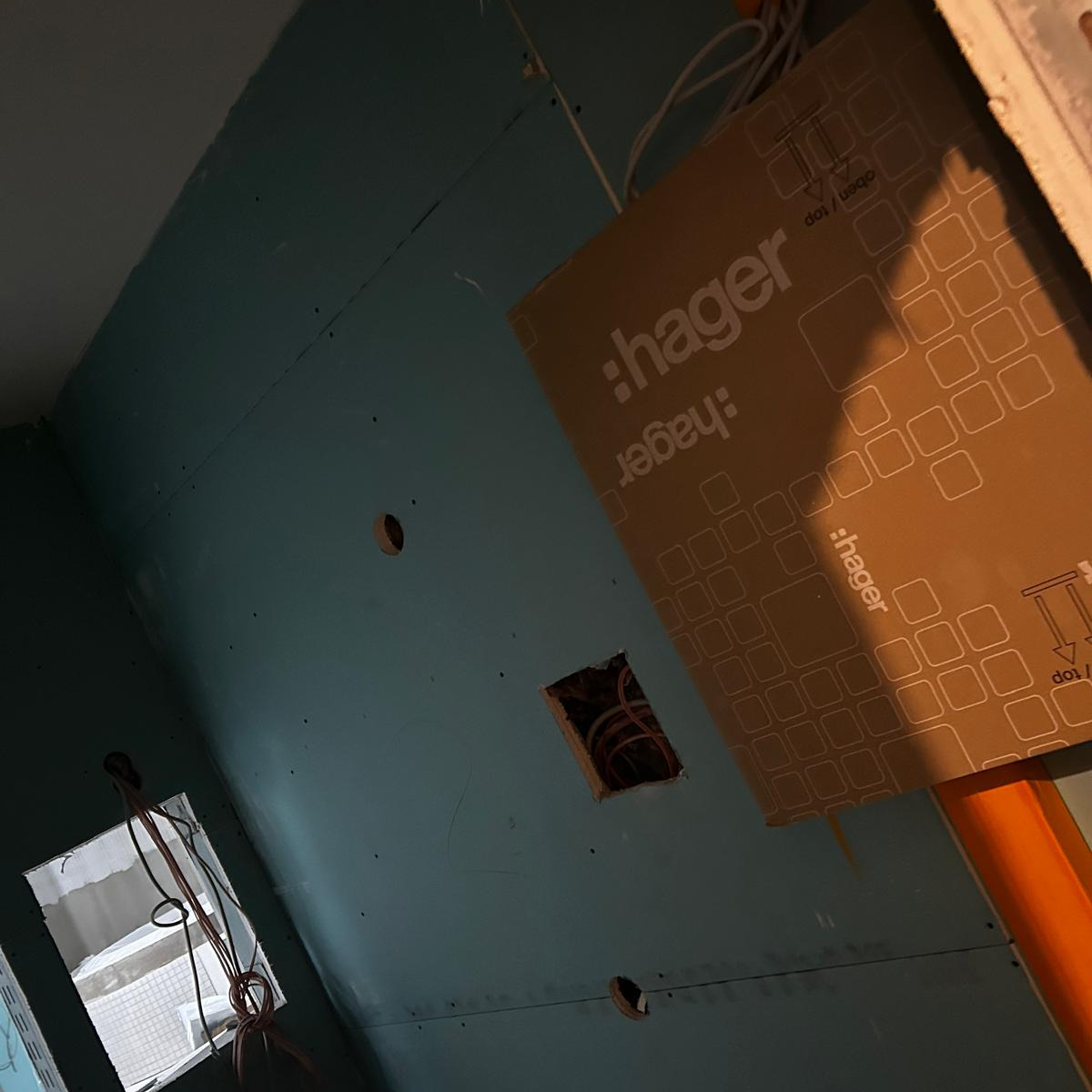 Niebieska płyta gipsowo-kartonowa z widocznymi otworami na instalacje elektryczne i puszkę Hager, w trakcie prac wykończeniowych.