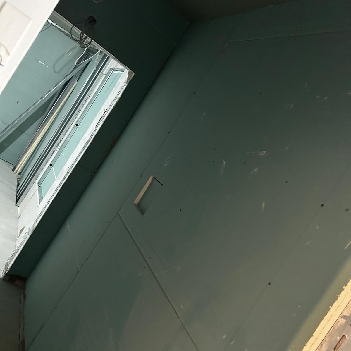 Wnętrze w Holtensen z zamontowanymi płytami gipsowo-kartonowymi na ścianach i suficie, widoczne otwory i wystające przewody elektryczne.